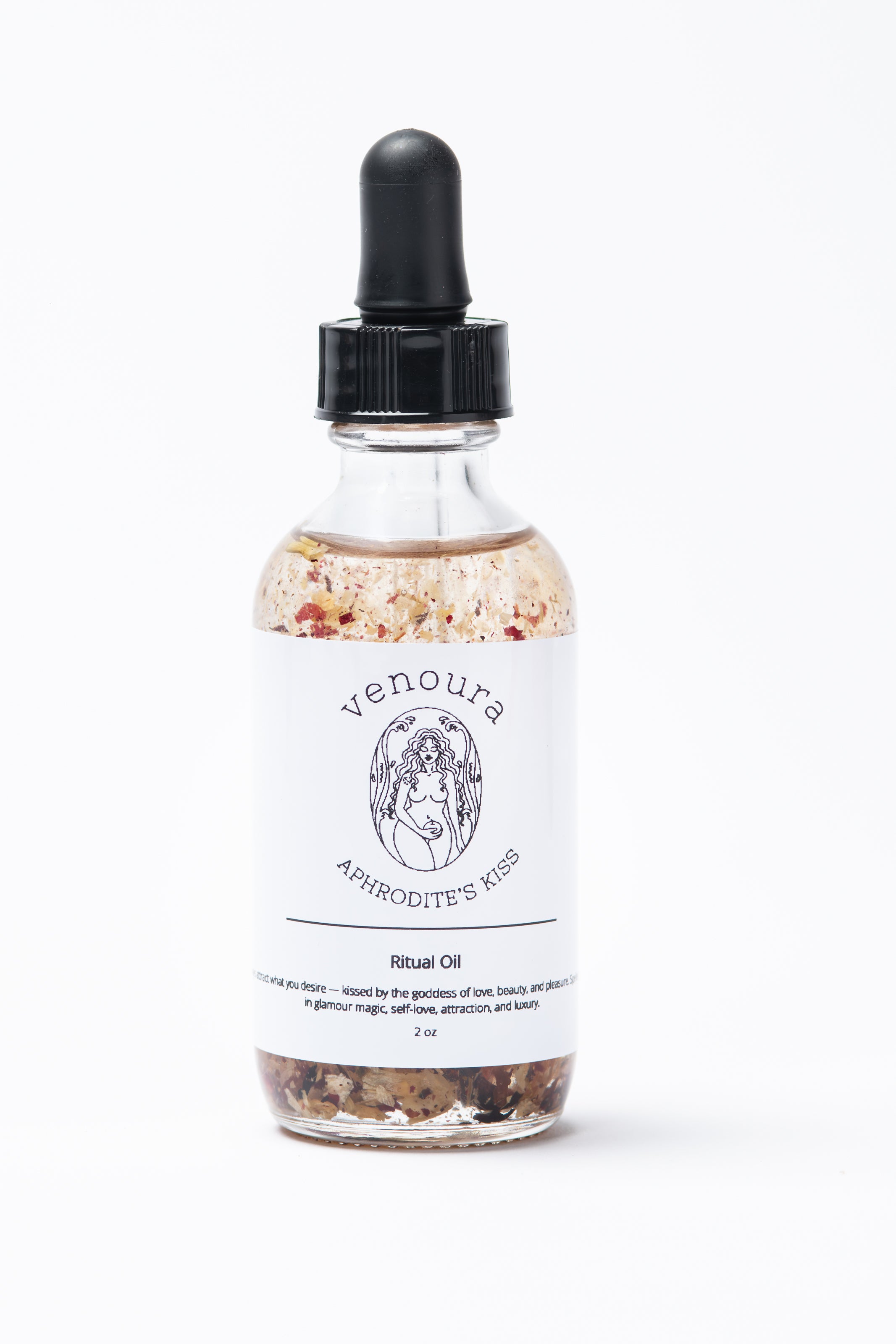 Venoura Aphrodite's Kiss Ritual Oil in a clear glass dropper bottle with a white label and black cap, filled with oil and suspended botanicals, on a white background.