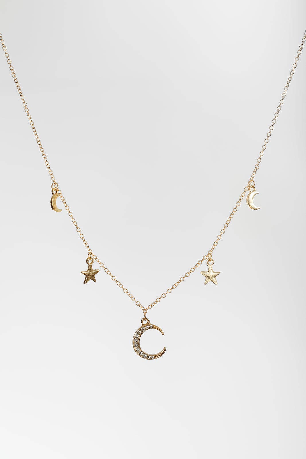 A delicate gold chain necklace featuring small celestial charms, including three crescent moons and two stars, with one larger crescent moon charm embellished with small clear stones, displayed against a light gray background.