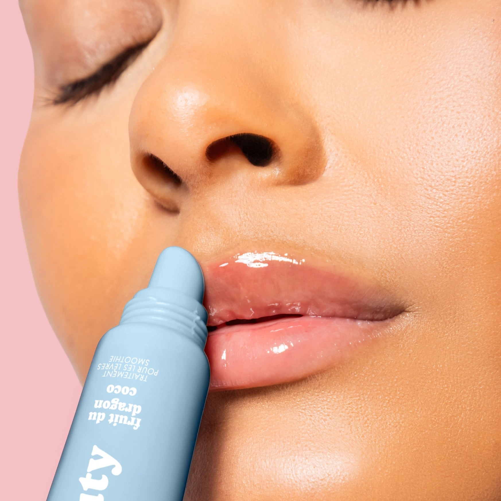Person applying a blue lip balm to their lips with a pink background
