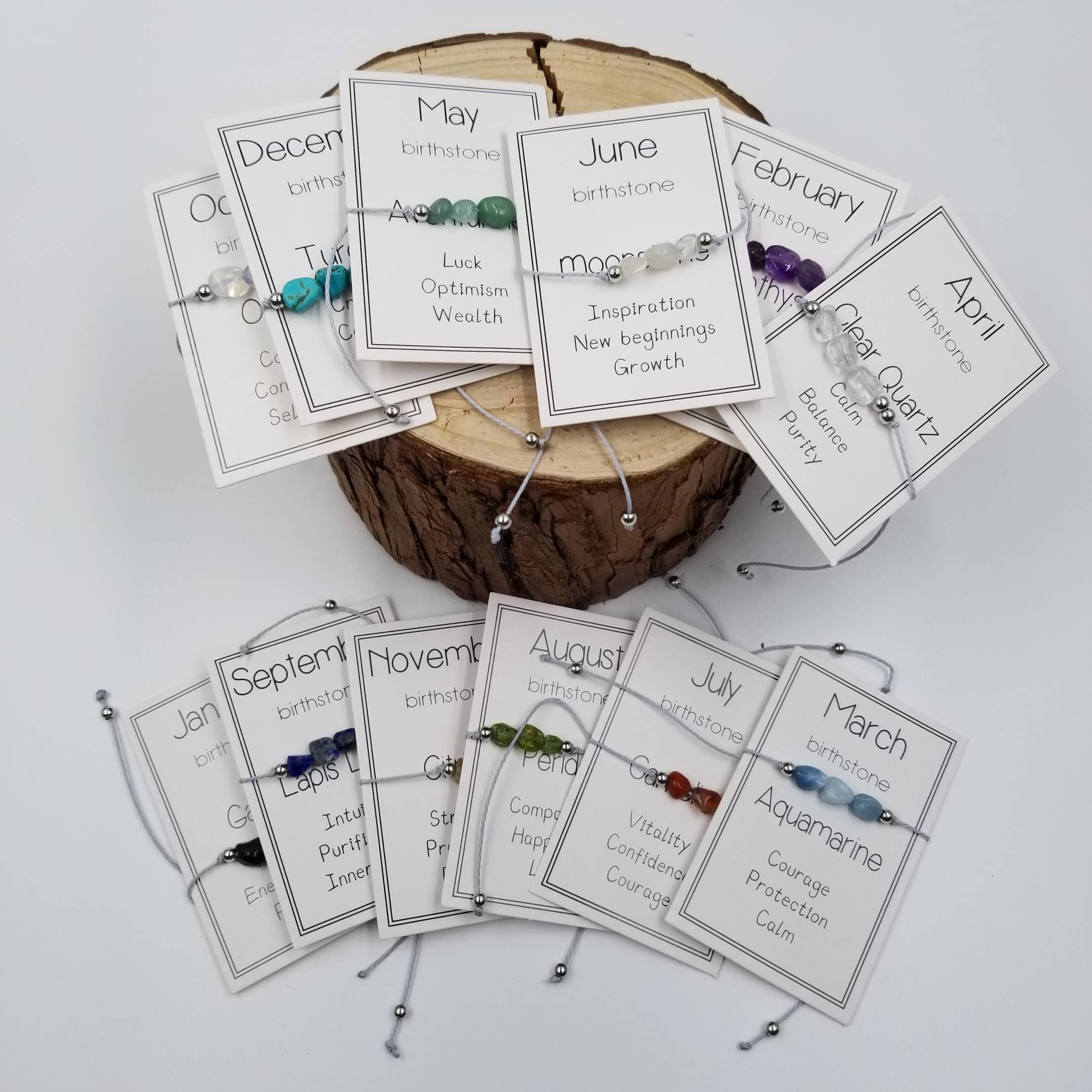 Collection of birthstone bracelets with corresponding cards on a wooden block and white surface.