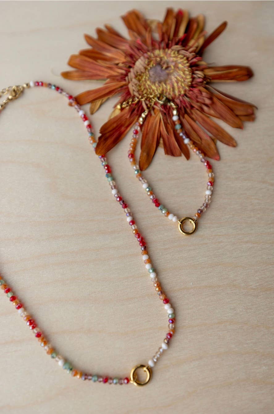 Beaded necklace with gold accents and a dried flower on a wooden surface