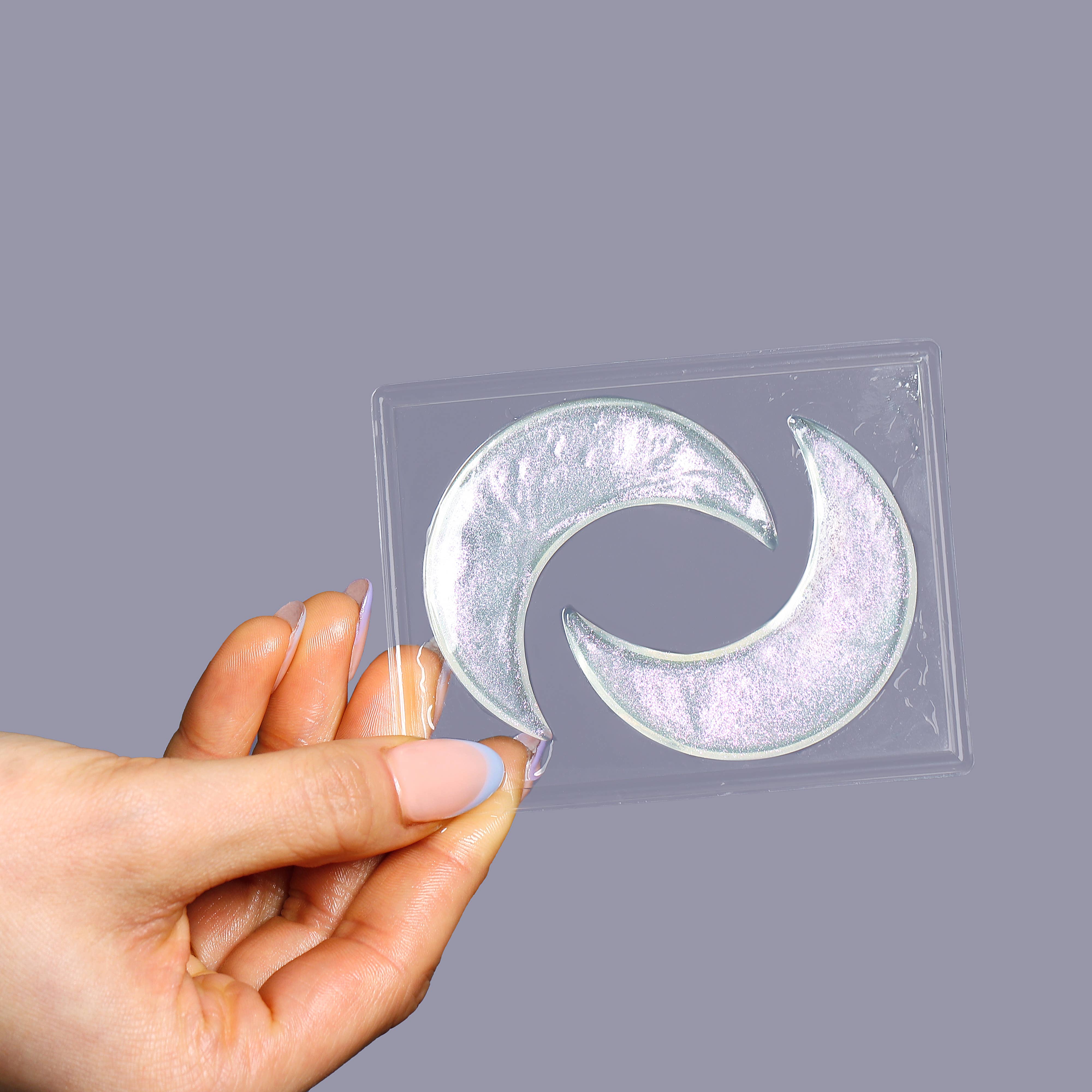 Hand holding a clear square sheet with a circular design on a gray background