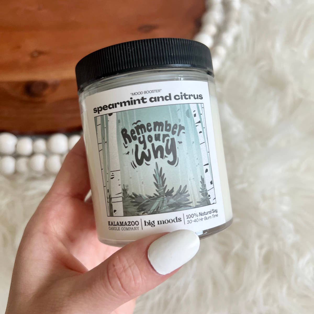 Hand holding a candle jar labeled 'spearmint and citrus' with a decorative label on a textured surface.
