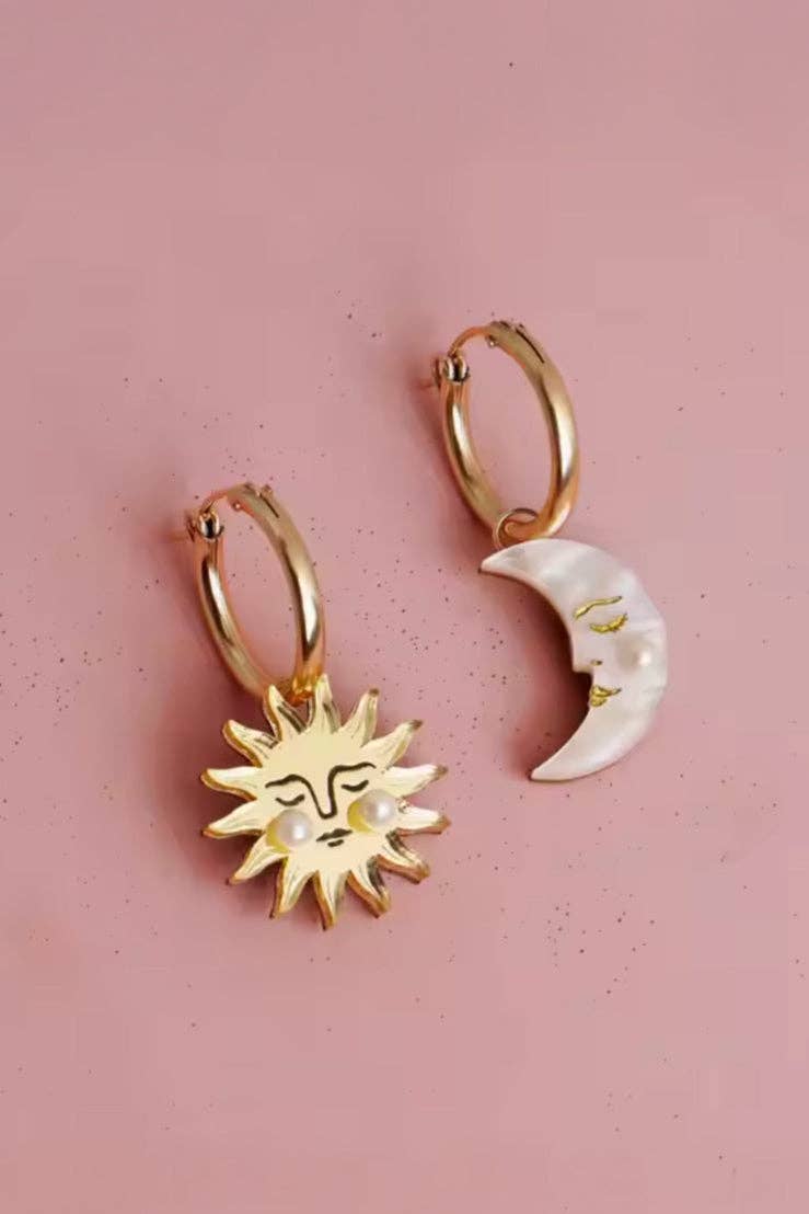 Gold hoop earrings with sun and moon charms on a pink background