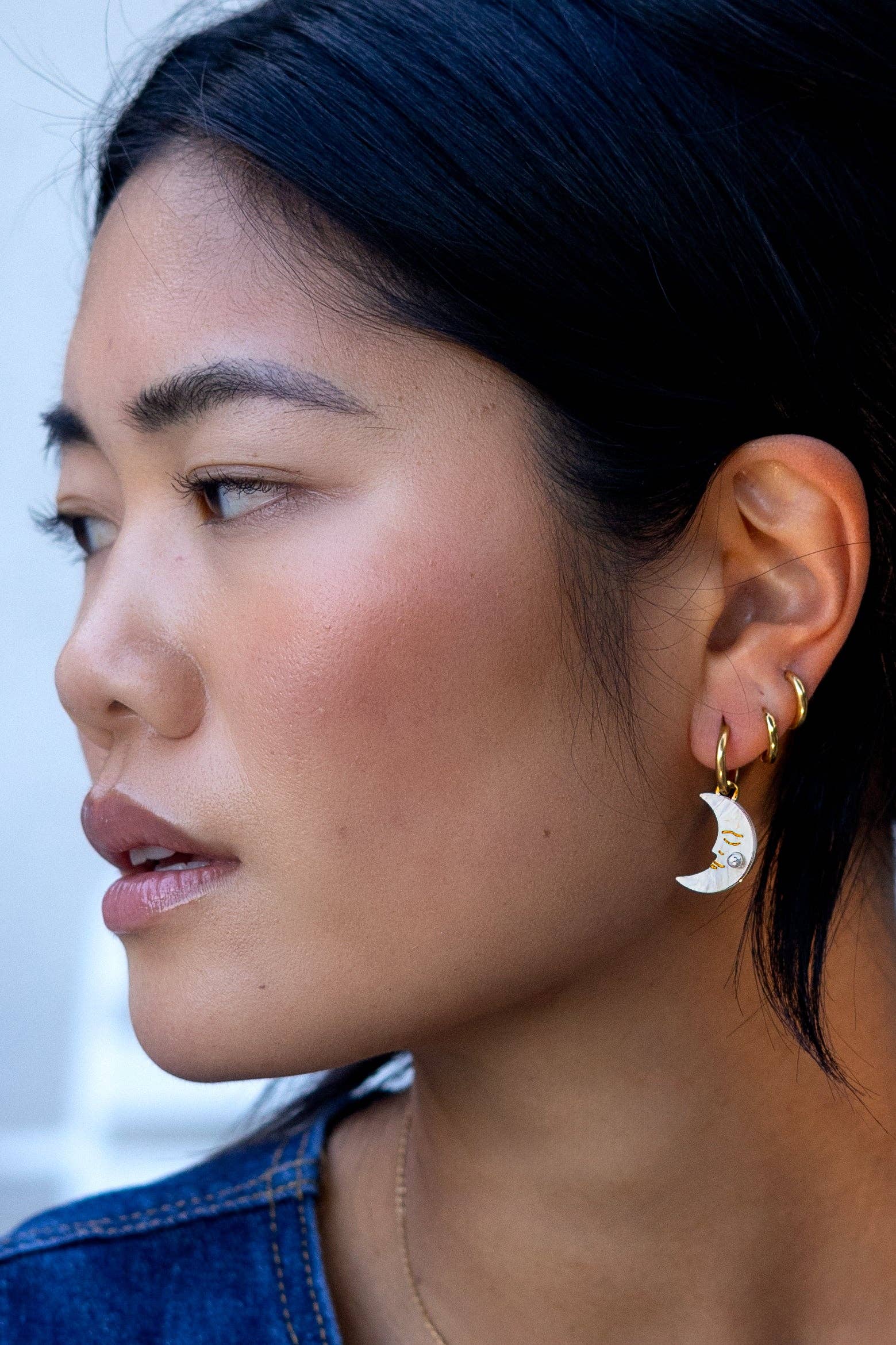 Close-up of a person wearing gold hoop earrings with moon designs.