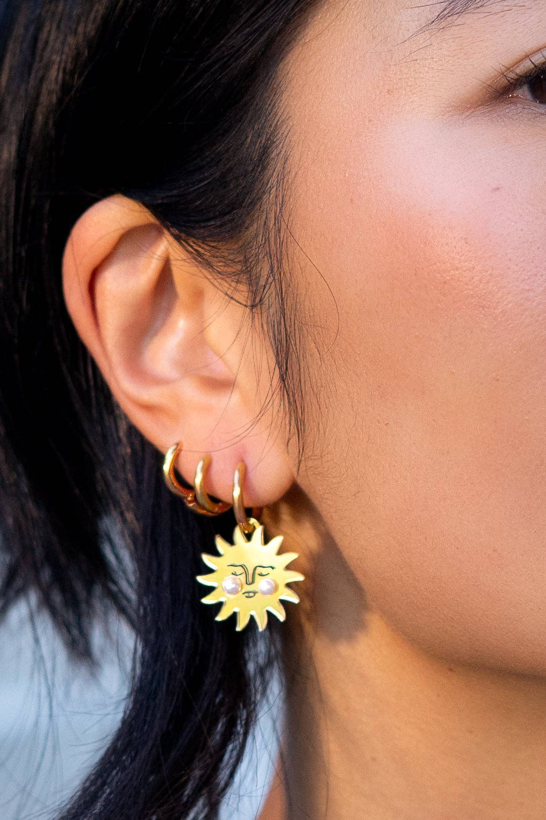 Close-up of a person wearing gold hoop earrings with a sun-shaped earring.