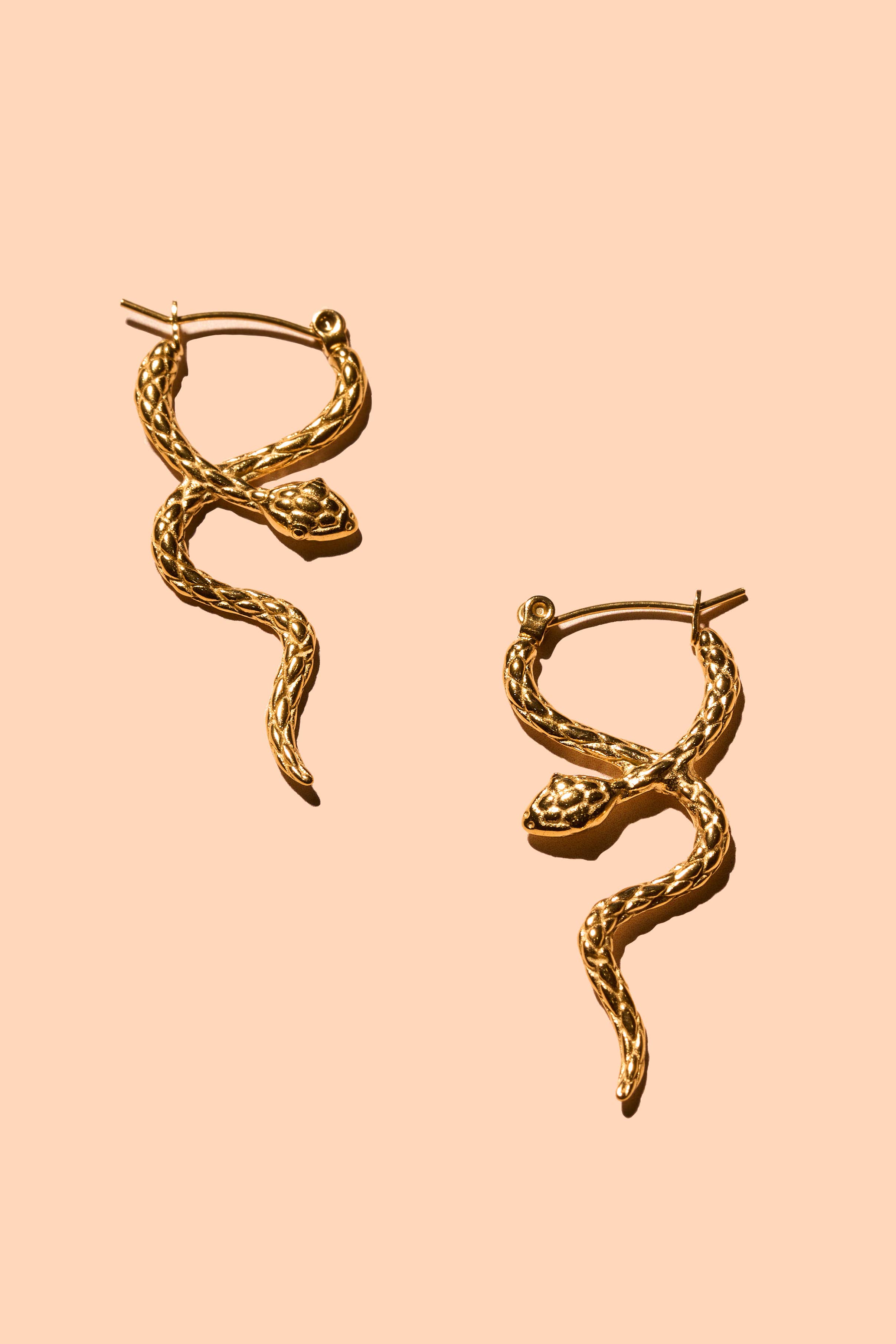 Gold snake-shaped earrings on a peach background