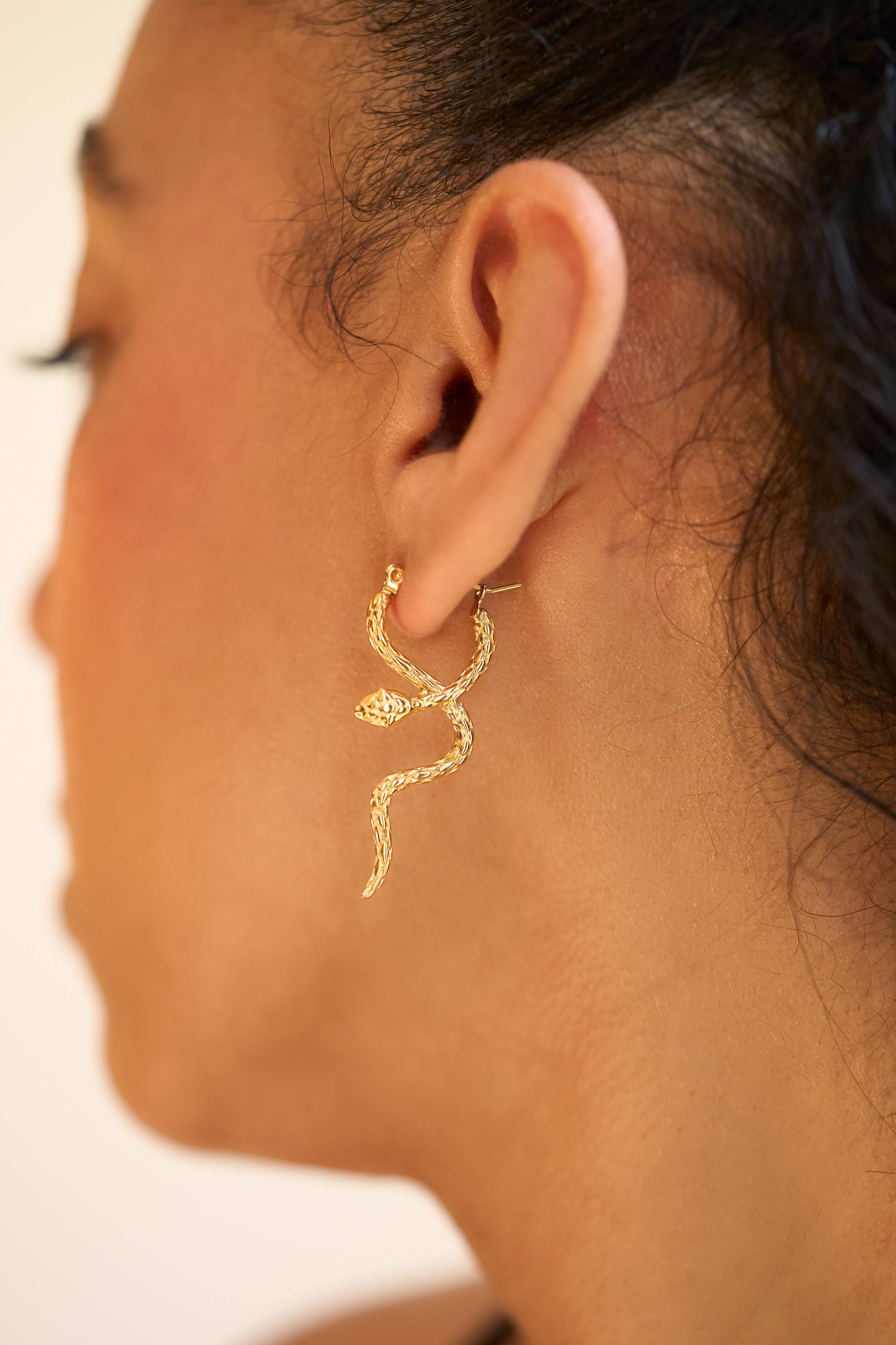 Close-up of a person wearing a gold snake-shaped earring.
