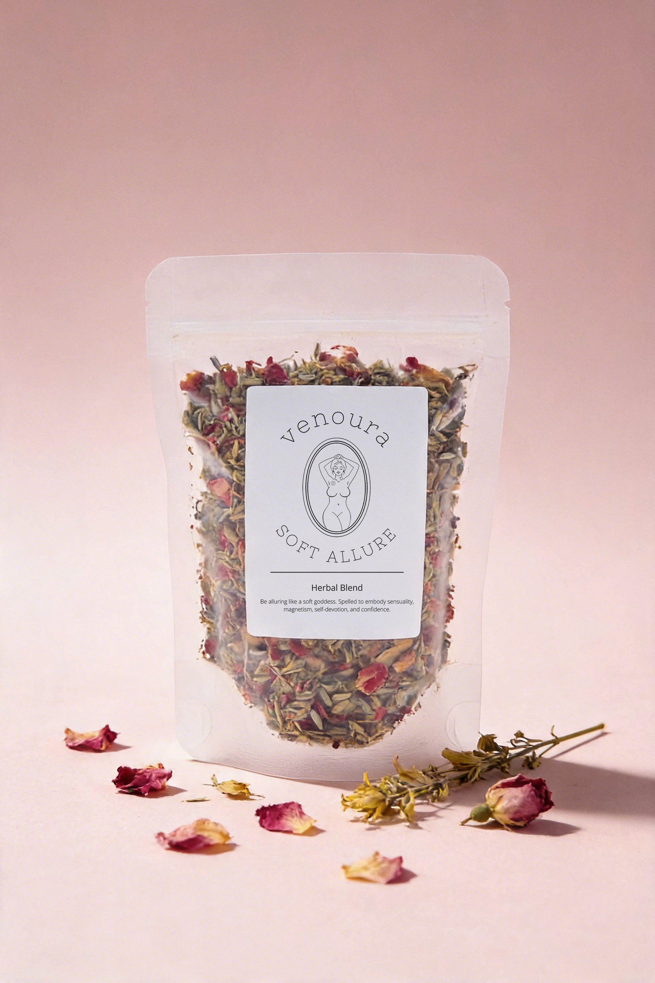A stand-up pouch of Venuura Soft Allure Herbal Blend shown on a soft pink background with scattered dried rose petals and a sprig around it. The pouch is clear enough to show the loose herbal contents inside, with a white front label displaying the brand name.