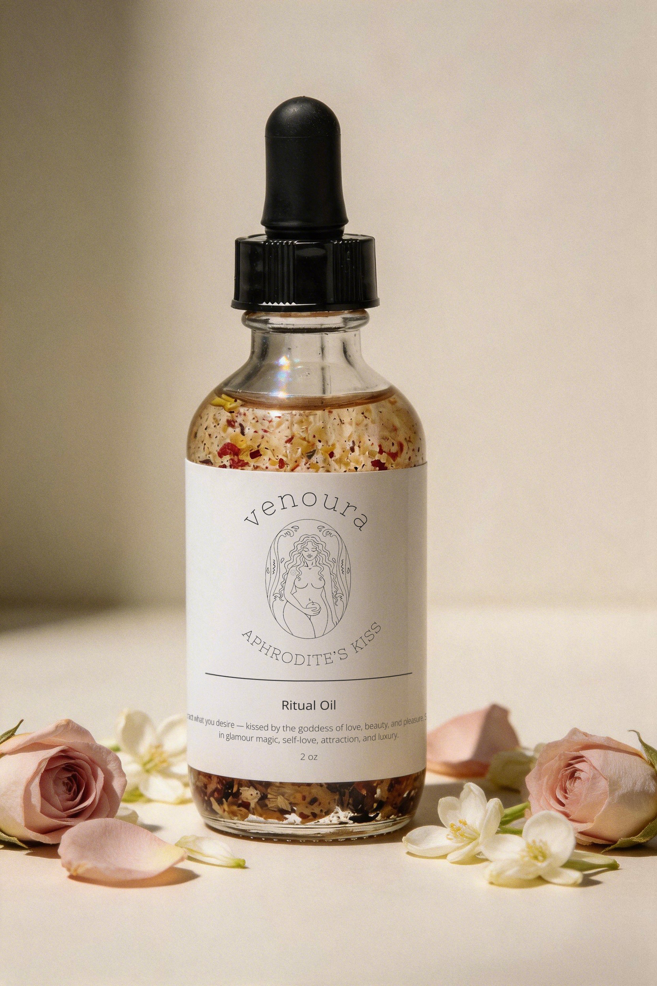 Venoura Aphrodisiac Ritual Oil in a clear glass dropper bottle with a black cap, surrounded by pink roses and white blossoms on a warm beige background.
