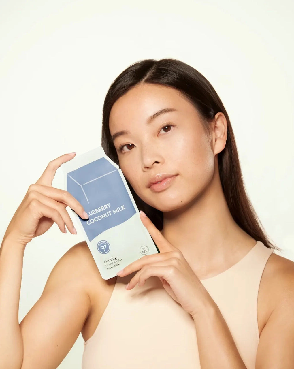 Woman holding a skincare product packaging against a plain background