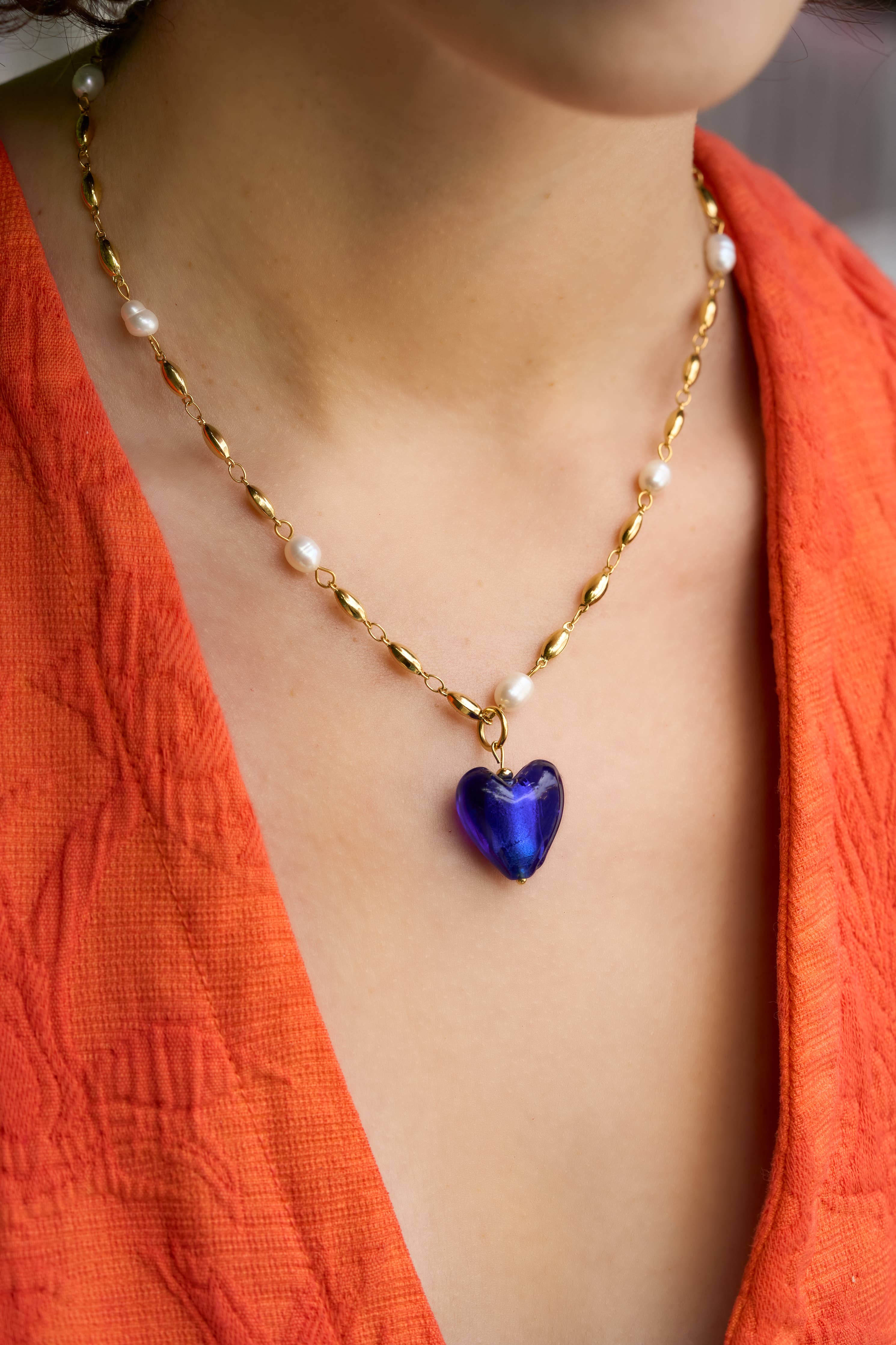 Necklace with a blue heart pendant worn by a person in an orange garment.