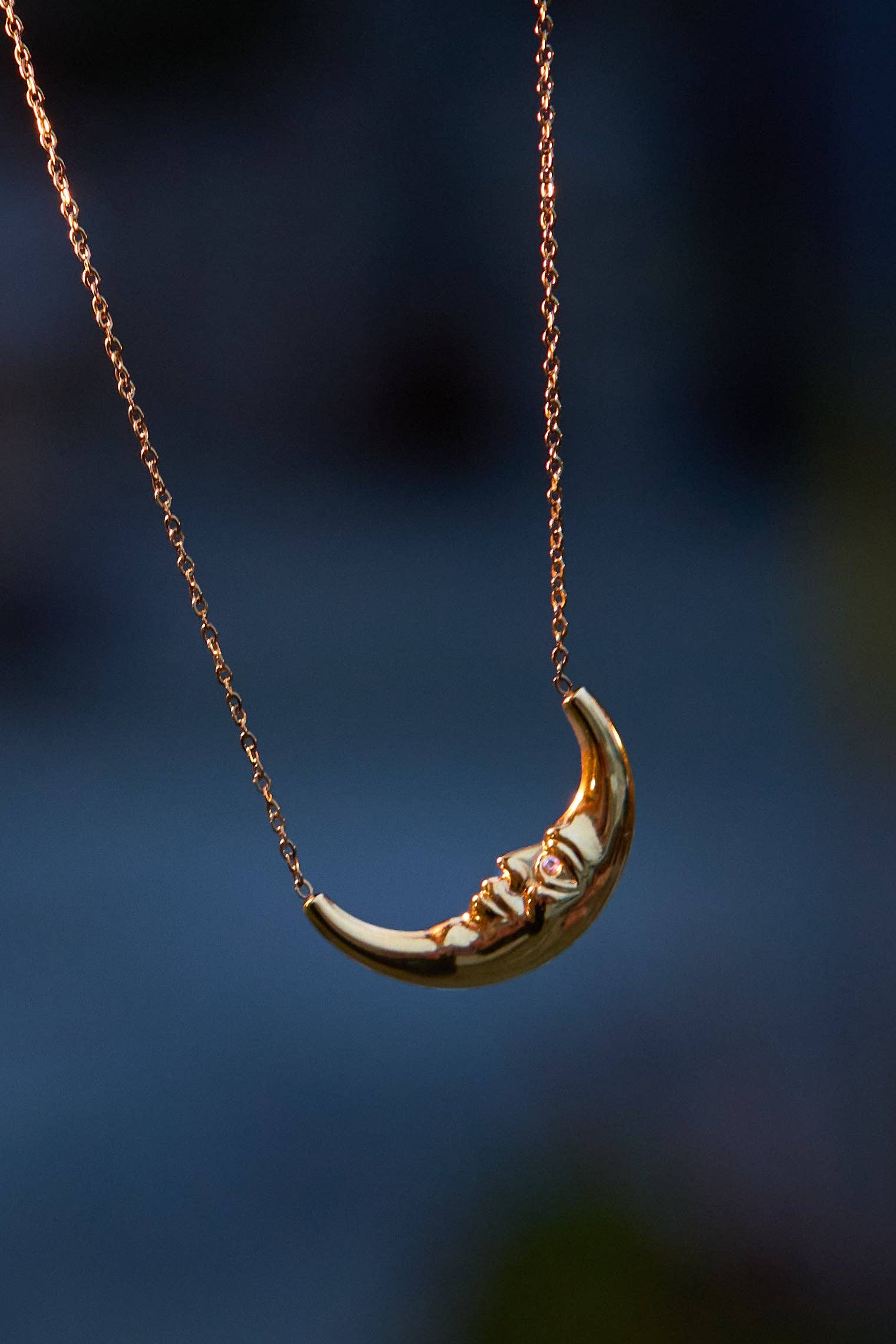 Gold crescent moon necklace on a dark blue background