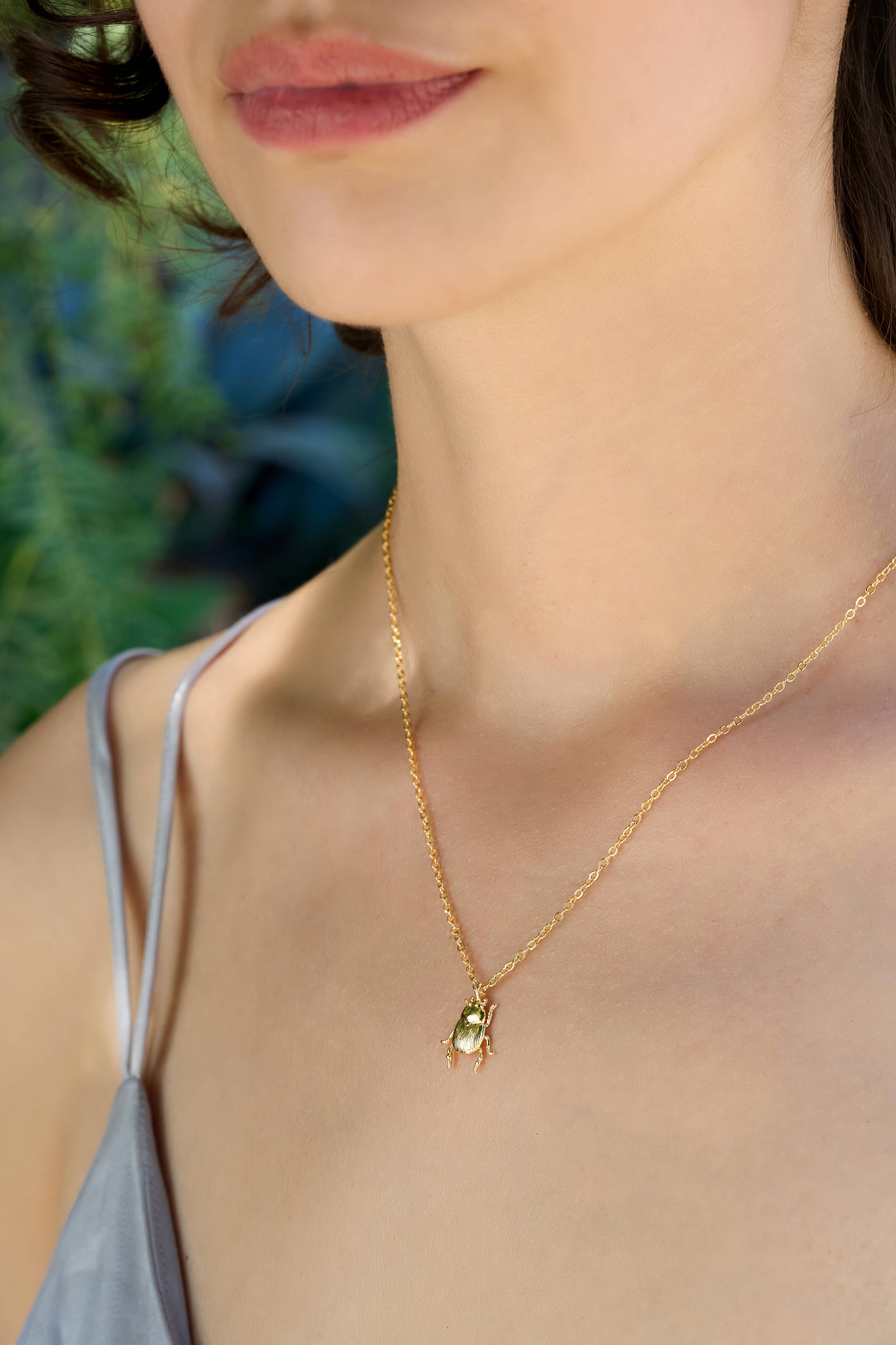 Close-up of a person wearing a gold necklace with a green pendant.