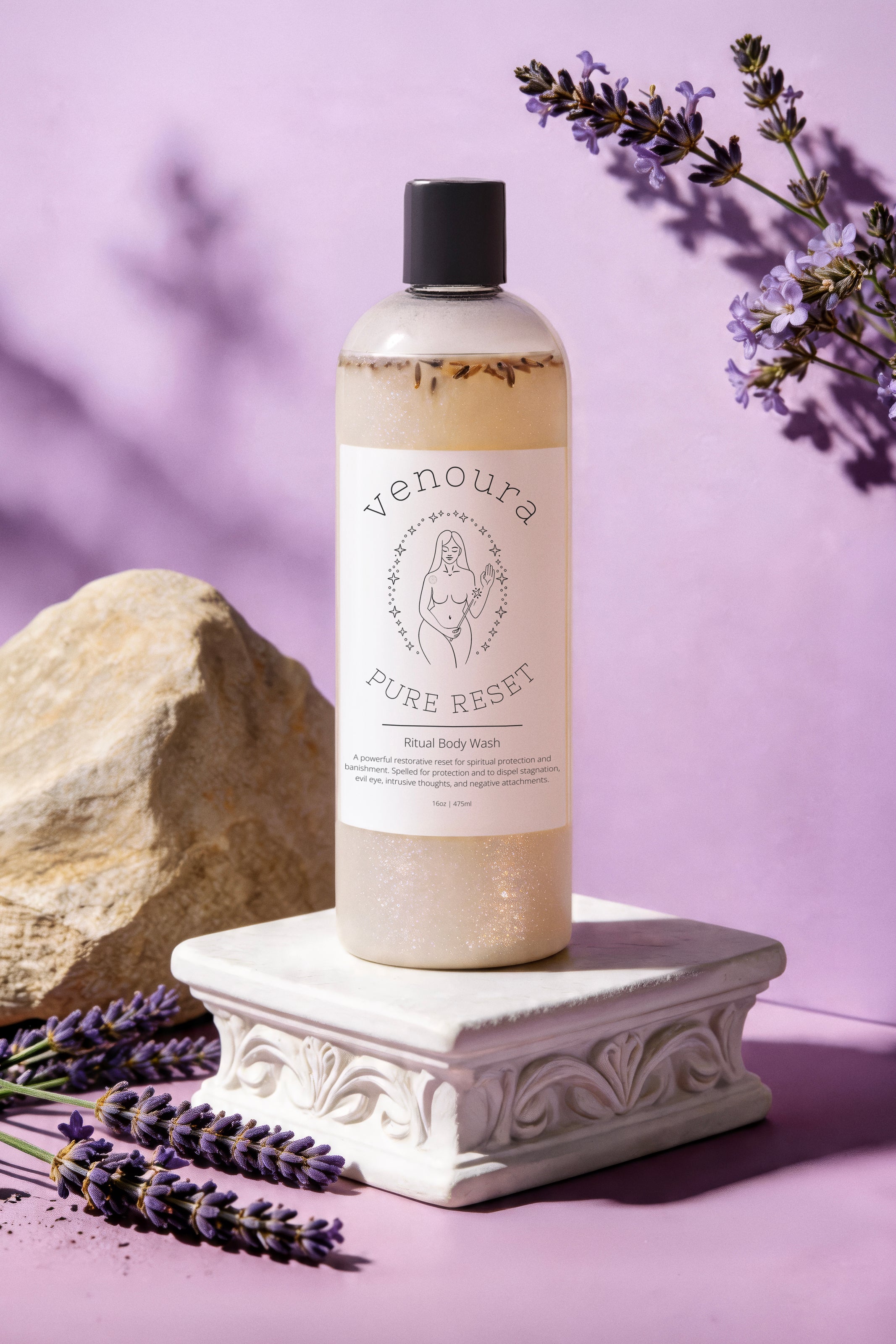 Venoura Pure Reset Herbal Body Wash in a clear bottle with a black cap, displayed on a white decorative pedestal. The scene is styled with lavender sprigs, a beige rock, and a soft purple background.