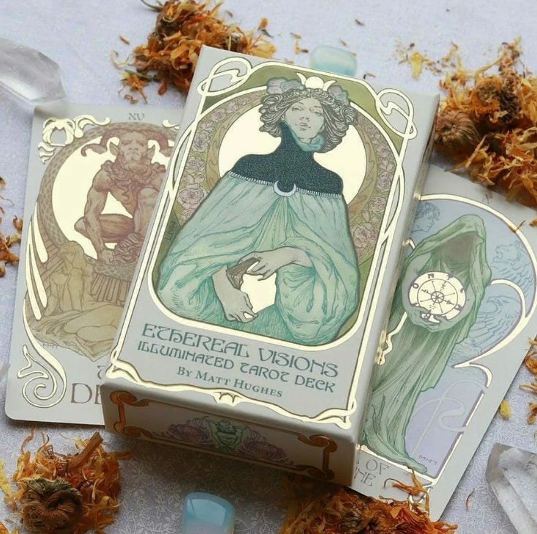 The box and cards of the Ethereal Visions Illuminated Tarot Deck by Matt Hughes, styled with dried orange flowers and crystals on a light gray surface.