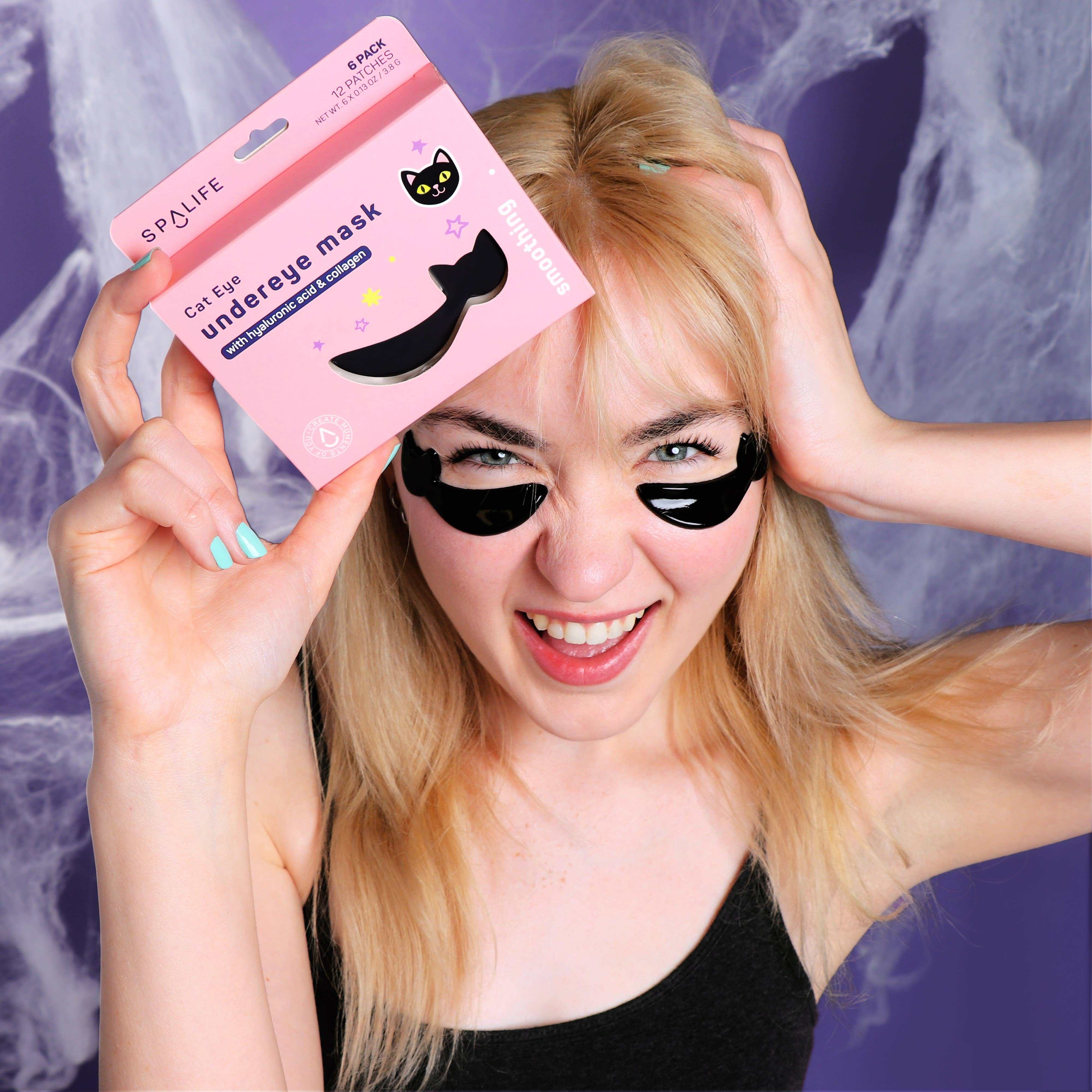 Woman holding a pink 'Spa Life' eye mask packaging with a black cat design against a purple background.
