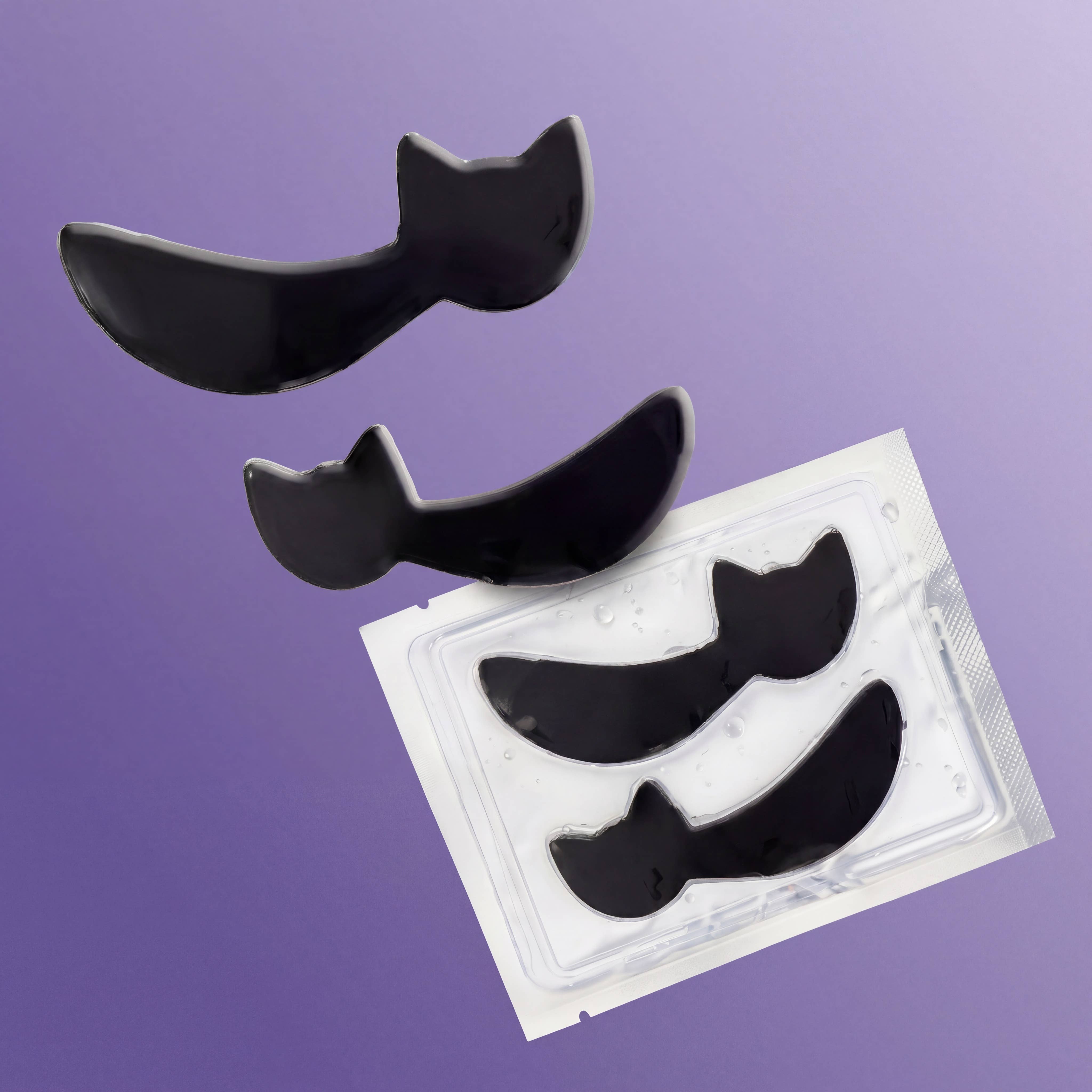 Three black curved eye patch pads shown above a clear plastic package containing additional patches, set against a solid lavender-purple background.
