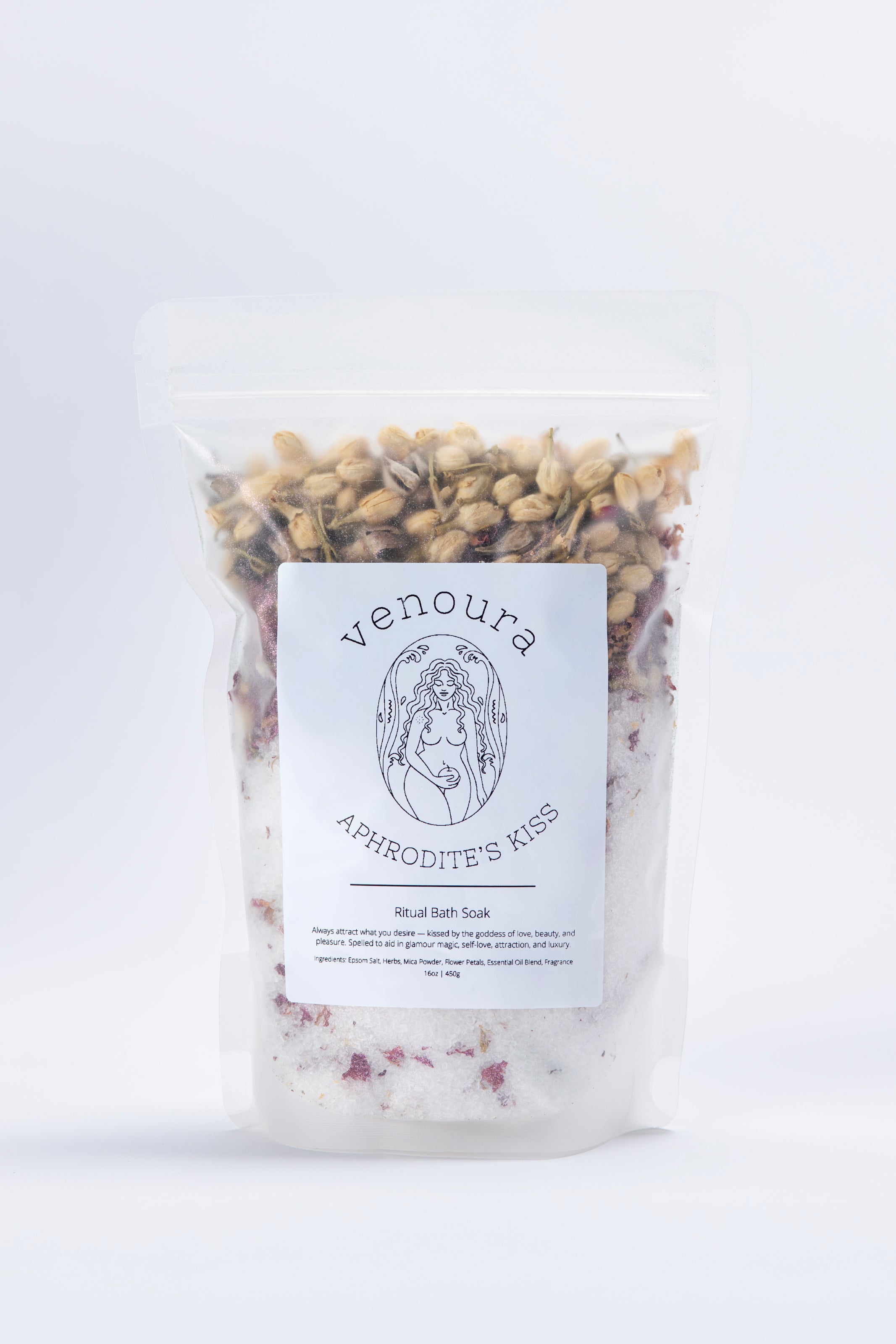 Venoura Aphrodite's Kiss Bath Soak in a clear stand-up pouch with a white label, showing dried flowers and white bath salts inside, on a white background.