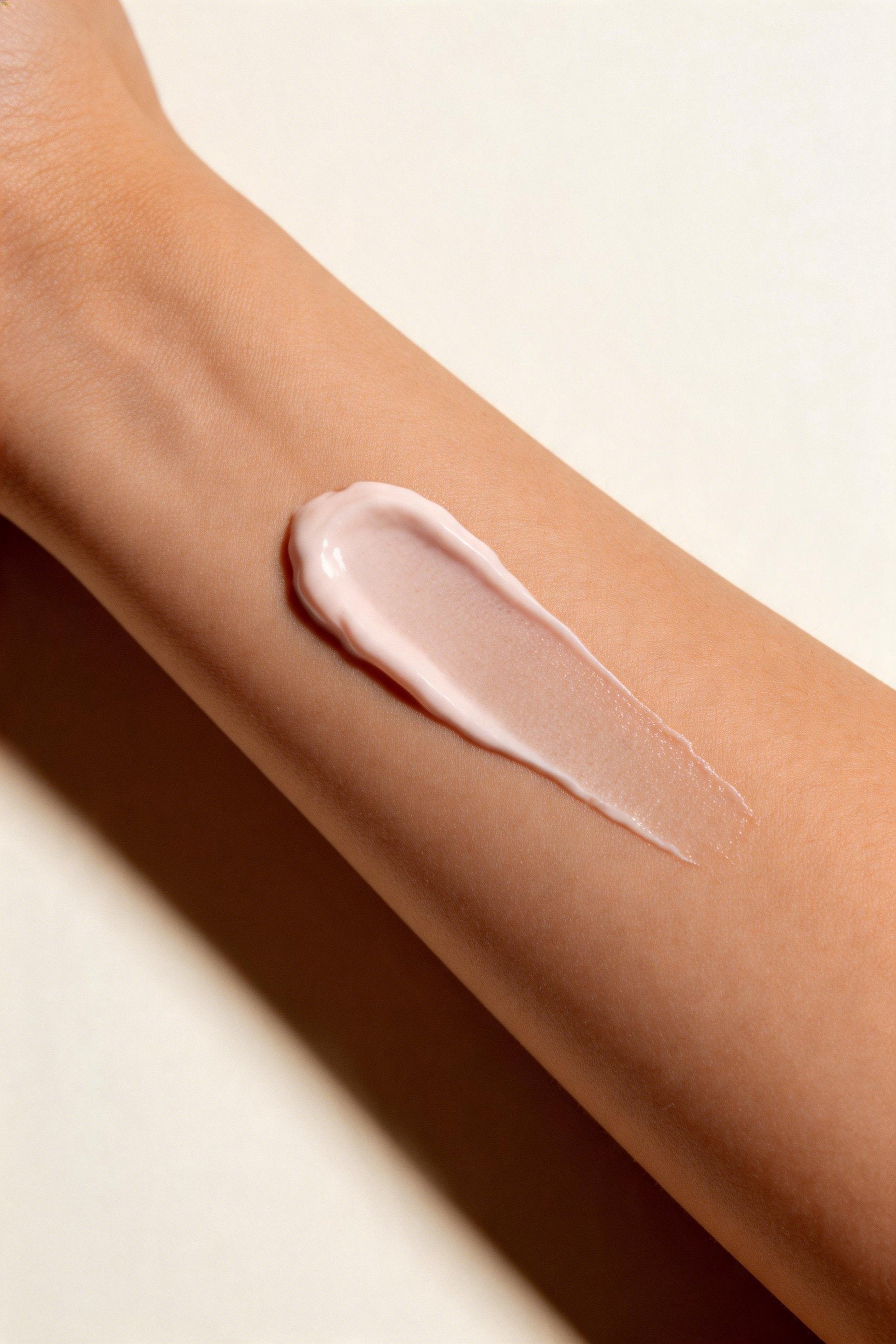 A thick, smooth smear of pale pink cream or lotion applied to a person's forearm against a warm off-white background.