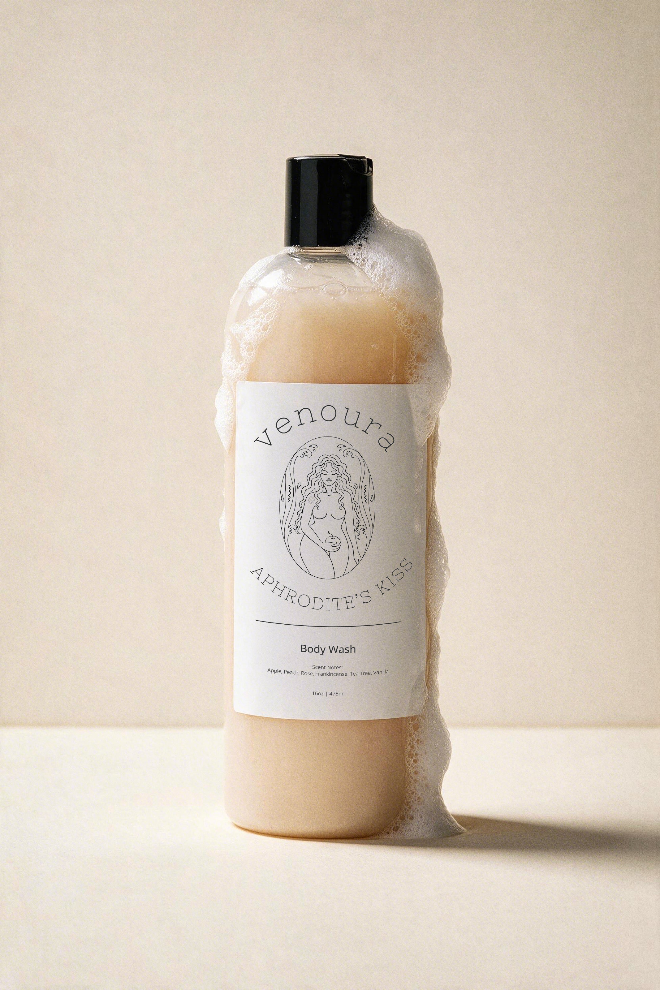 Venoura Aphrodite's Kiss Body Wash in a frosted bottle with a black cap, shown with thick lather foam against a warm beige background.