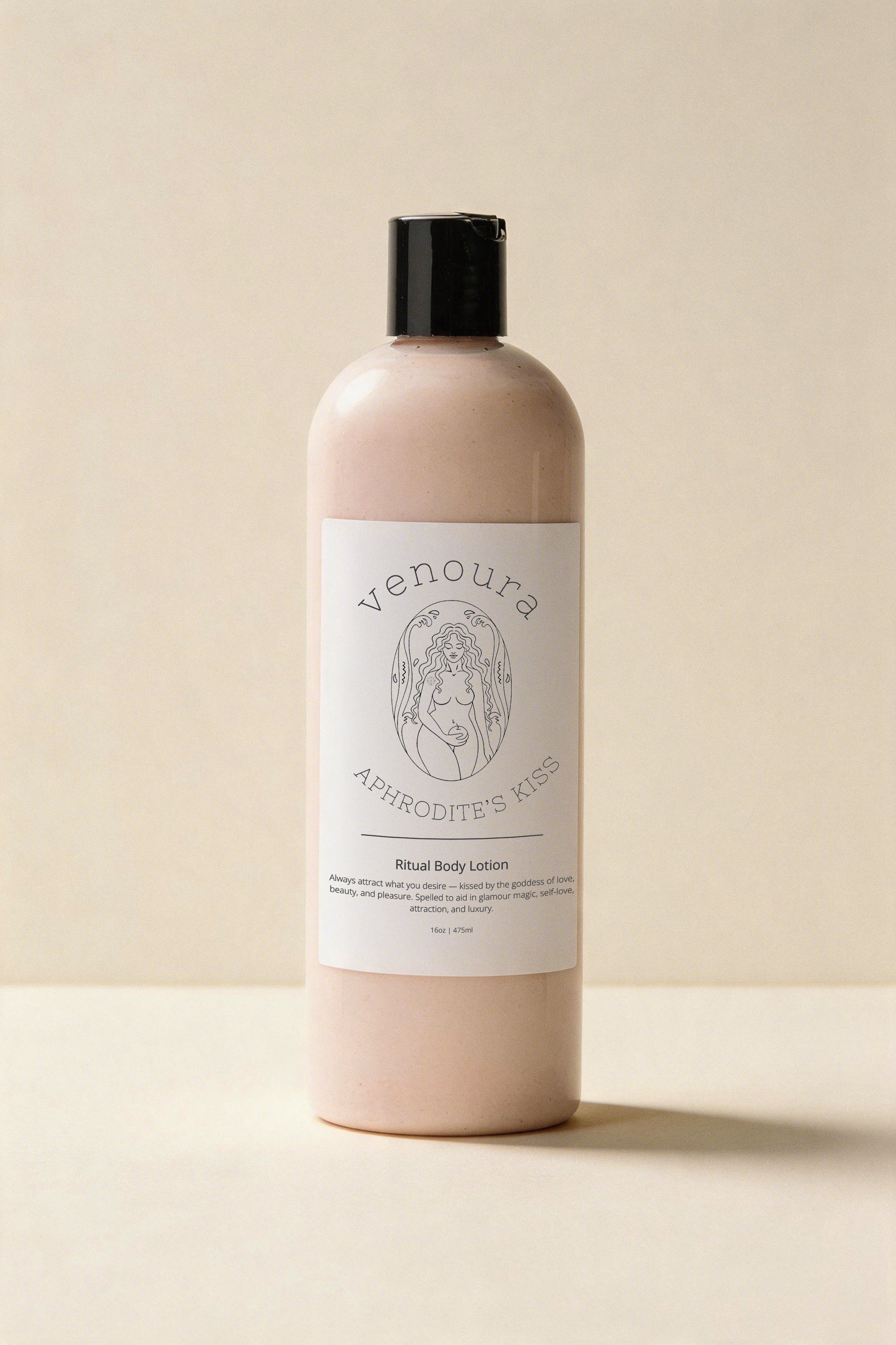 Venoura's Aphrodite's Kiss Ritual Body Lotion used for beauty, attraction, self-love, luxury, glamour, magic, skin-nourishing, moisturizing in a pale pink bottle with a black cap and white label, set against a warm beige background.