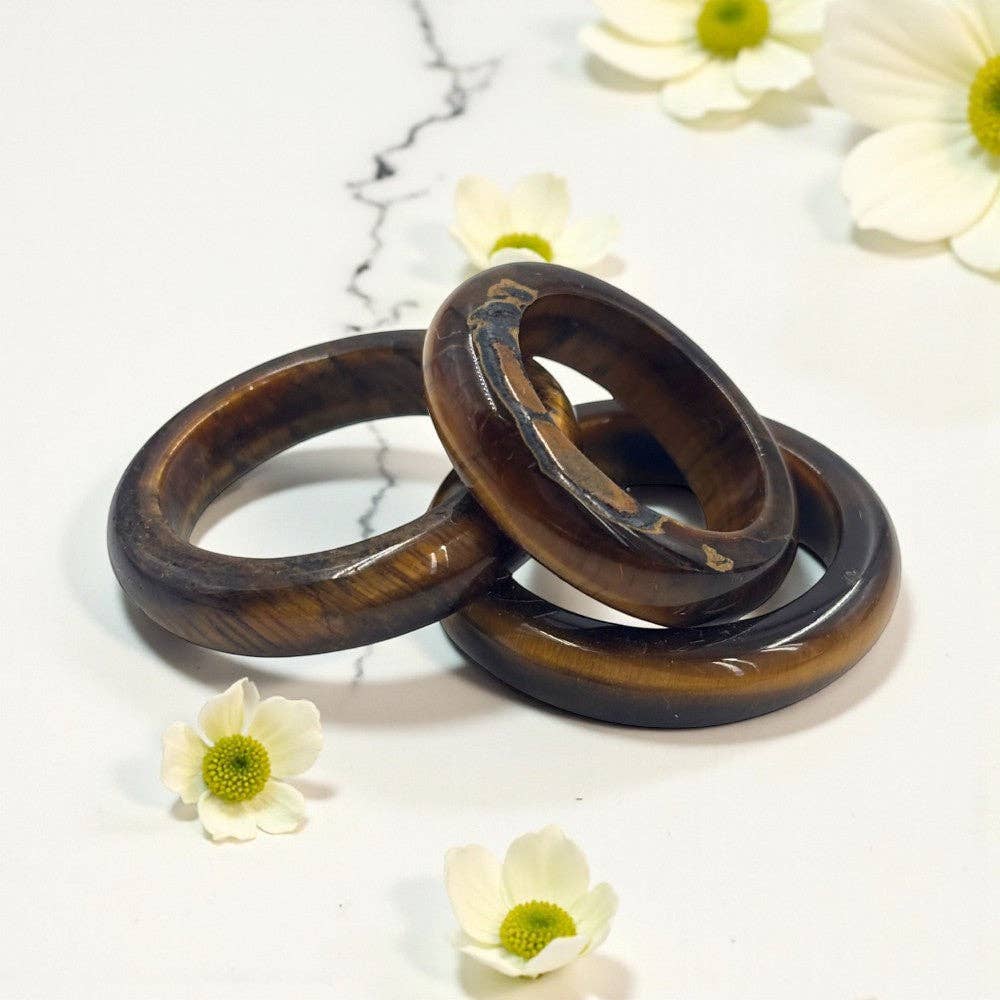 Tiger's eye crystal bands stacked on a white surface with white flowers around them. 