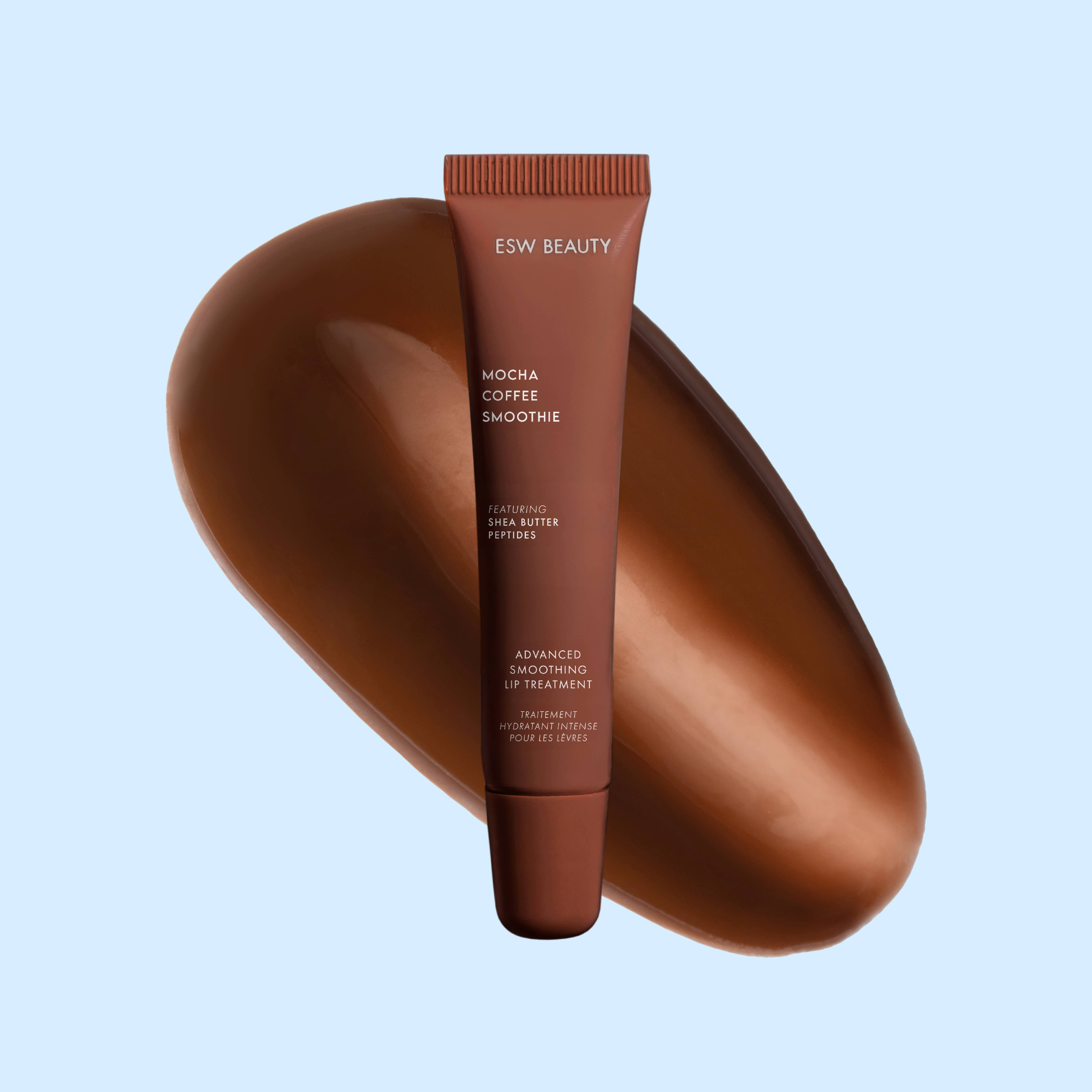 A squeeze tube of ESW BEAUTY Mocha Coffee Smoothie face butter positioned in front of a large, glossy, curved brown smear on a light blue background.