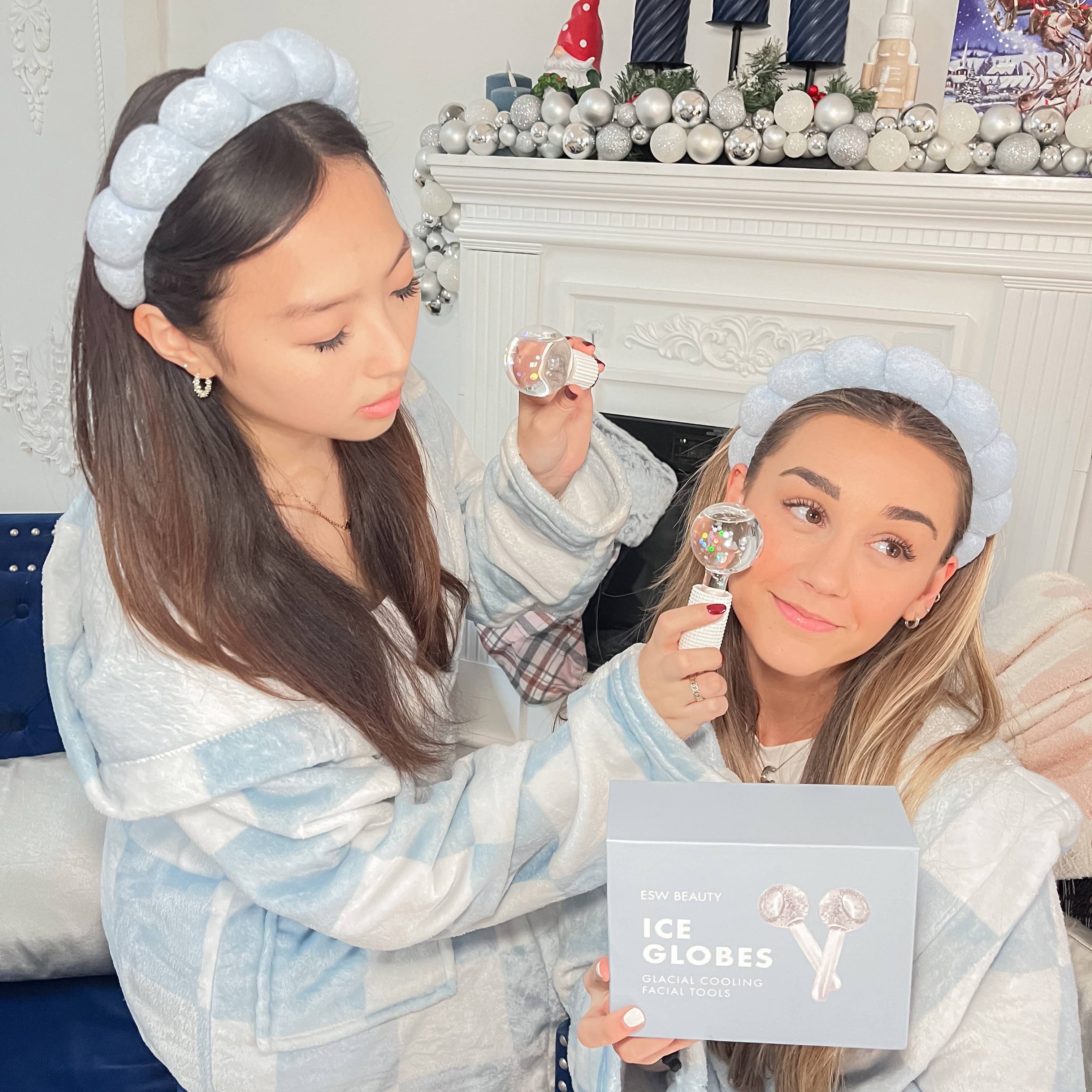 Two women wearing ice globe headbands in a festive room with Christmas decorations.