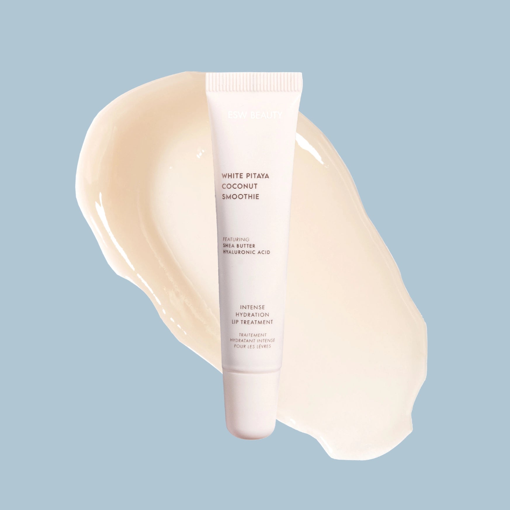 A white tube of Amrederm White Pitaya Coconut Smoothie lip treatment is centered over a glossy cream-colored swipe on a light blue background.